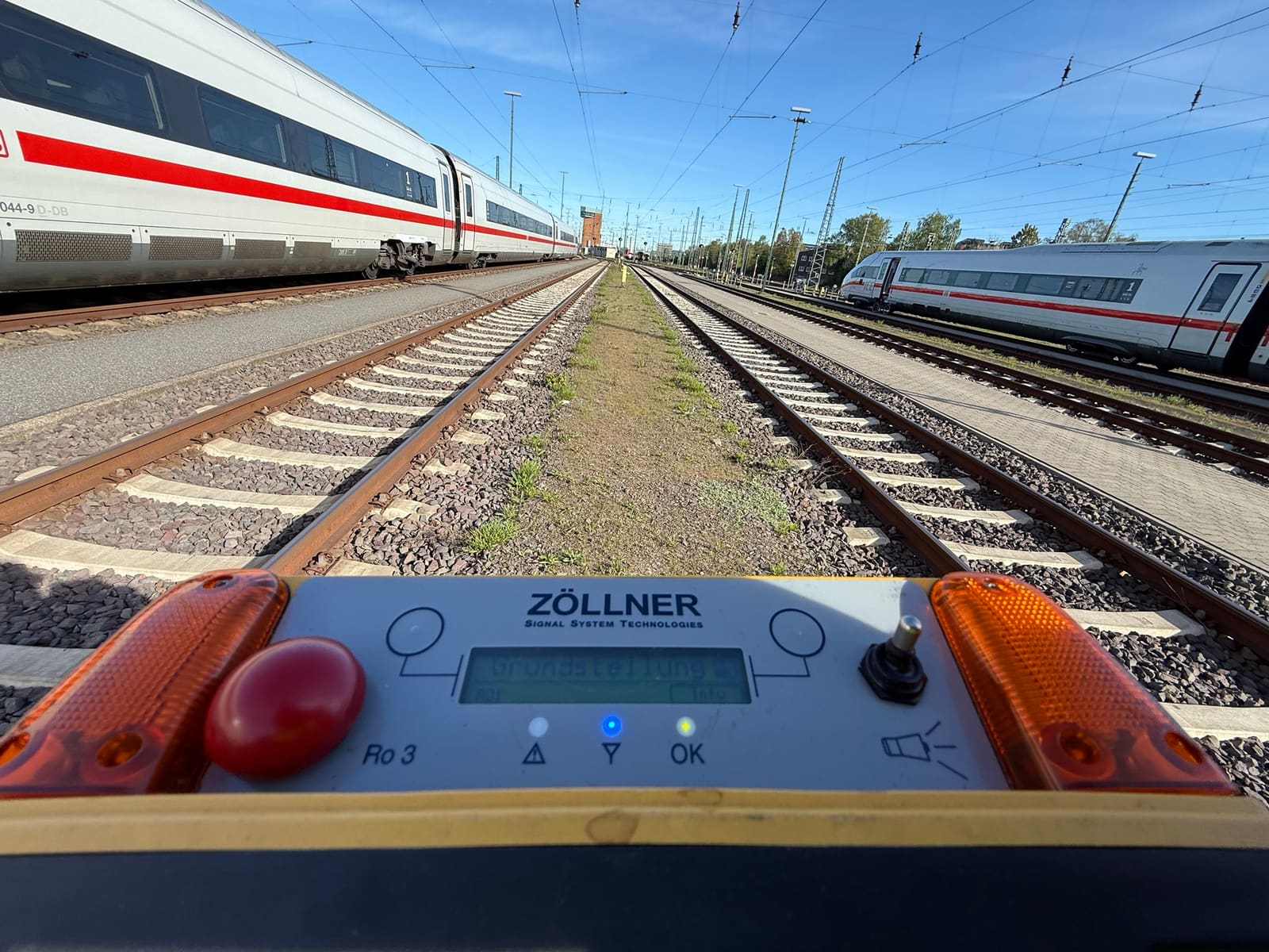 Warngerät der Sicherungsanlage zwischen zwei Gleisen, daneben ICE-Züge