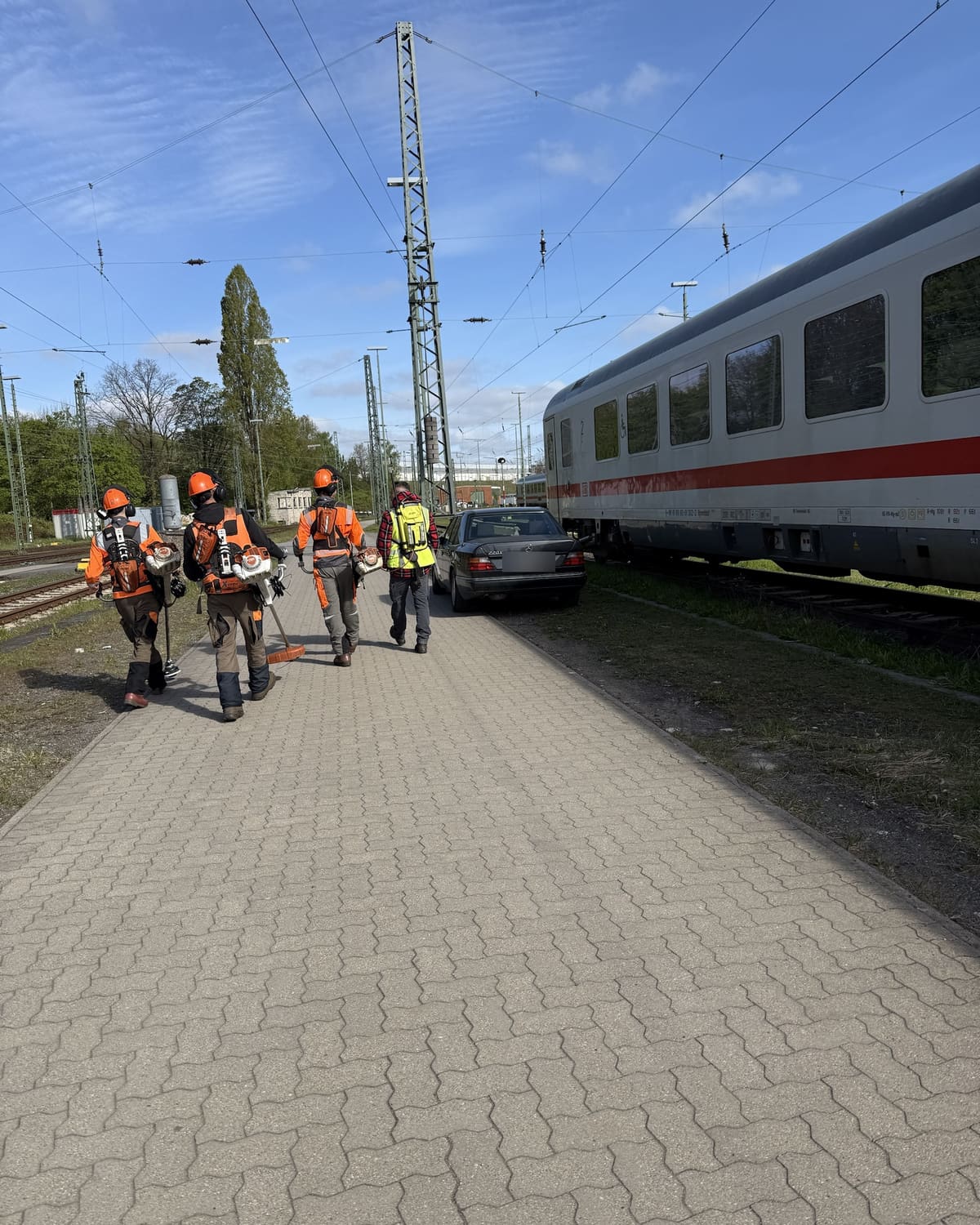 BBG-Sicherungsposten in Warnweste begleitet eine Arbeitskolonne über den Bahnsteig